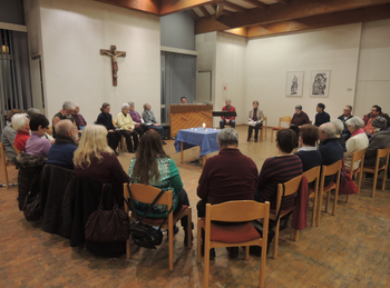 Gebet für die Einheit der Christen Menschen sitzen im Stuhlkreis in einem Gemeindesaal und beten und singen gemeinsam. In der Mitte steht ein geschmückter Tisch mit einer Kerze.